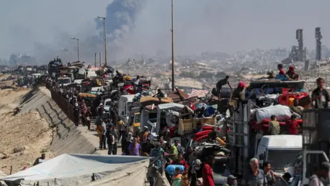 Reuters Smoke rises from an Israeli strike as displaced Palestinians flee northern Gaza, in the central Gaza Strip (14 September 2025)